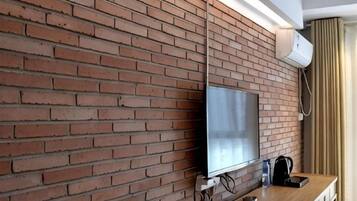 A brick wall with a flat-screen TV mounted on it, a wooden table, and a black bag on the table.