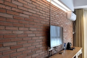 Un mur de briques sur lequel est fixé un téléviseur à écran plat, une table en bois et un sac noir posé sur la table.