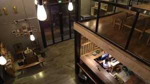 Een modern interieur met een houten vloer, een bar met een aanrecht en krukken, en een zithoek met tafels en stoelen.