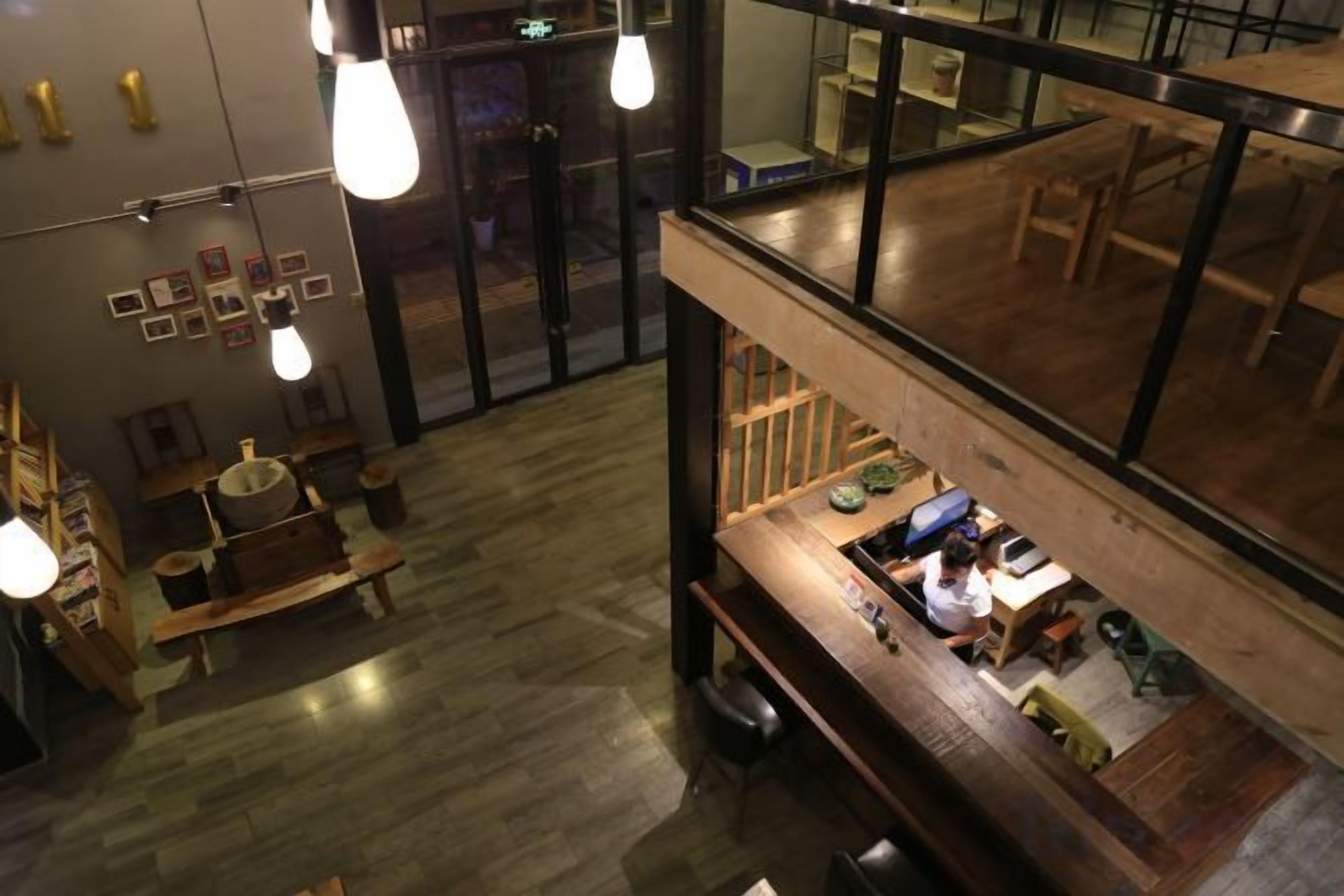 An interior view of a restaurant with a wooden bar area, hanging light fixtures, and a view through a glass partition.