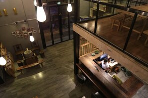 An interior view of a restaurant with a wooden bar area, hanging light fixtures, and a view through a glass partition. - Pingtang Yazhoutao Craft Hotel (Yingbin Avenue) (Pingtang)