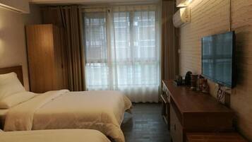 A hotel room with two beds, a wooden dresser, a flat-screen TV, and a window with sheer curtains.