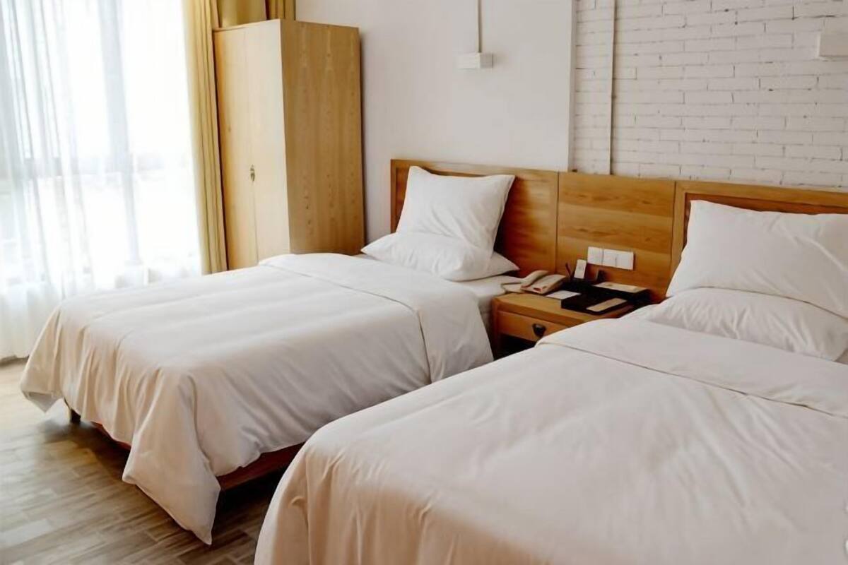 Ein Hotelzimmer mit zwei Betten, einem Holzschrank, einem Nachttisch mit Telefon und einer Backsteinwand.
