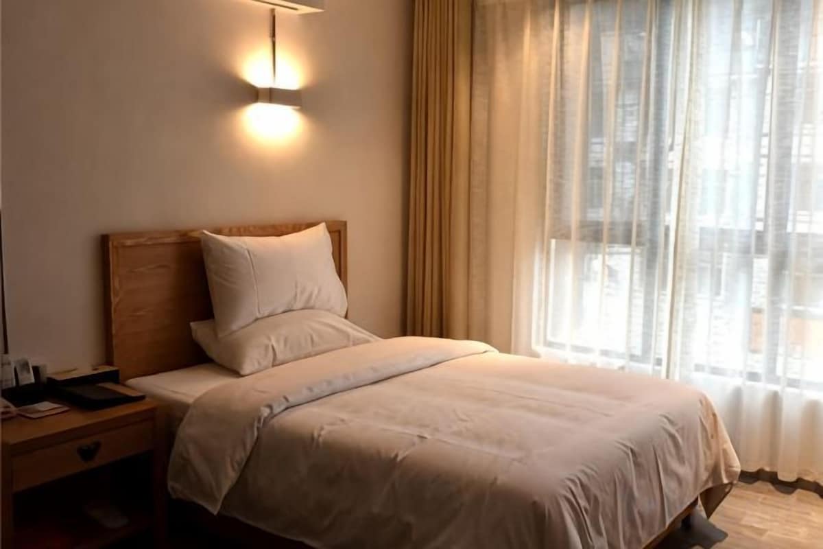 A hotel room with a bed, a bedside table, a lamp, and a window with curtains.