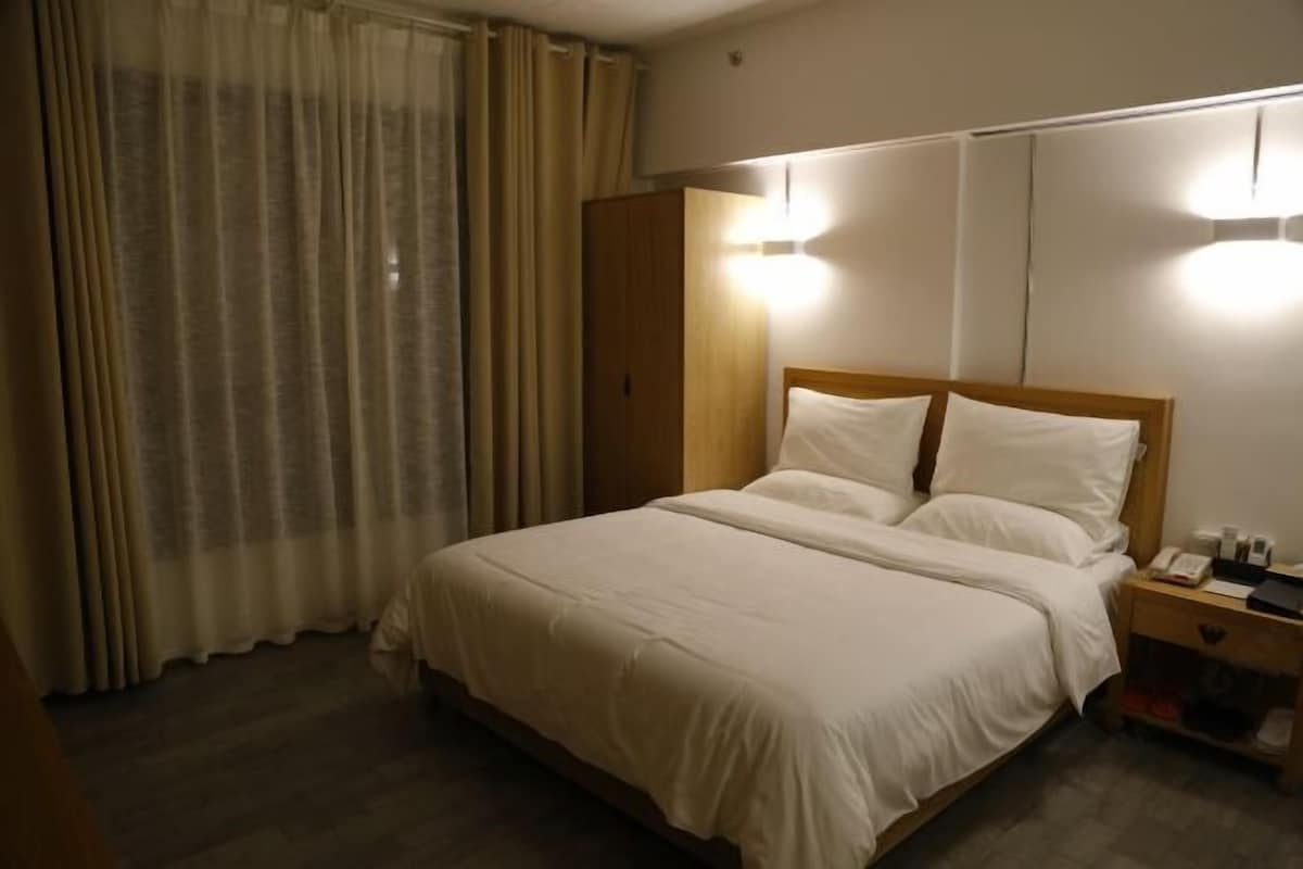 Quarto de hotel com cama, cortinas, mesa de cabeceira e guarda-roupa de madeira.