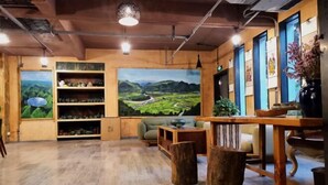 Een gezellige kamer met houten vloeren, een groot schilderij van een landschap, planken met decoratieve objecten en een tafel met een vaas.