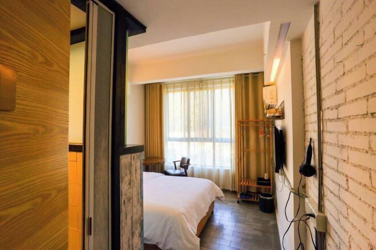 Ein Hotelzimmer mit Bett, Sessel, Wandfernseher und einem Fenster mit Vorhängen.