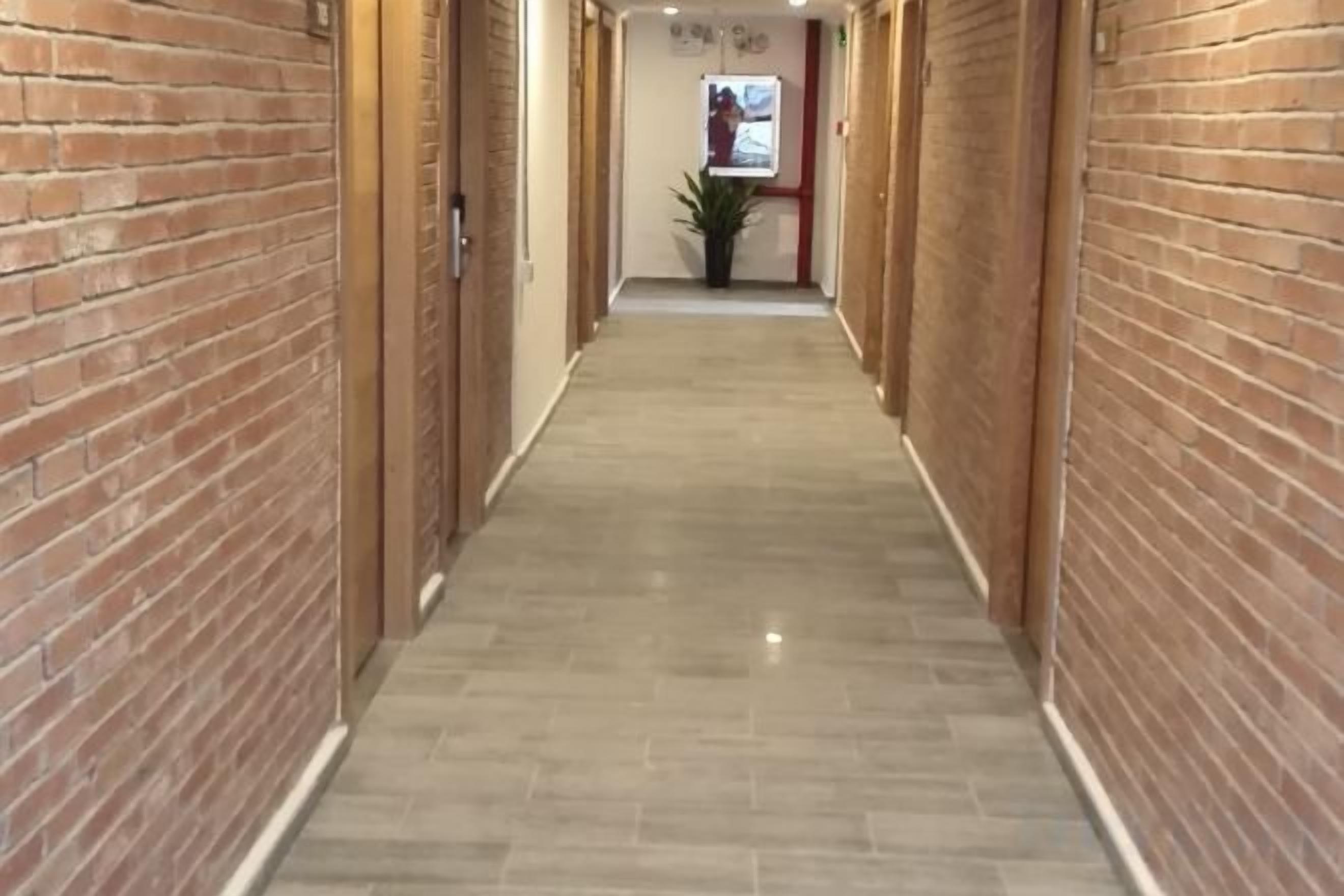 A corridor with brick walls and a tiled floor, leading to a door with a potted plant in the background.