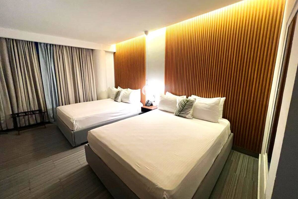 Une chambre d’hôtel avec deux lits, un mur recouvert de panneaux en bois et un rideau sur le côté gauche.