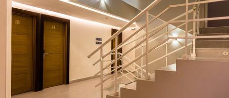 A modern staircase with a glass ceiling, wooden doors labeled 18 and 19, and a sign indicating room numbers 313-319 and 320-325.
