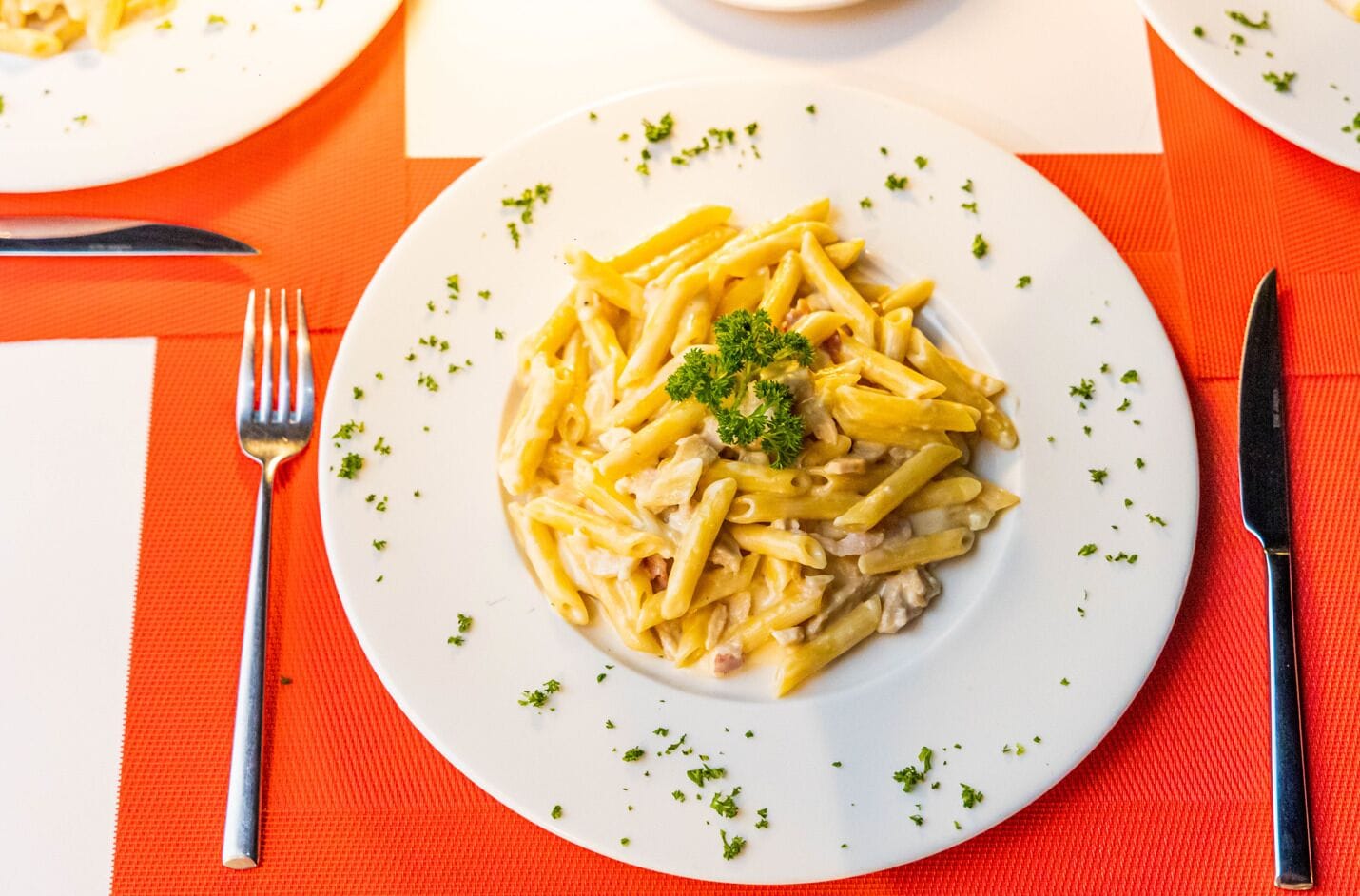 A plate of pasta with a garnish, placed on a table with a red placemat.