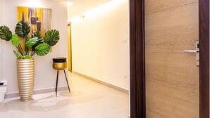 A hallway with a wooden door marked with the number 3, a large potted plant, and a small table with a basket. - Hotel Alkquimia (Bayahibe)