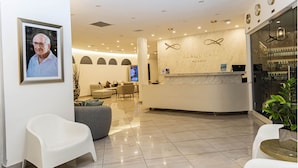 A modern reception area with a marble counter, a framed portrait on the wall, and a seating area with sofas and chairs. - Hotel Alkquimia (Bayahibe)