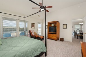 A bedroom with a four-poster bed, a ceiling fan, a television on a wooden cabinet, and a dining area with a table and chairs.