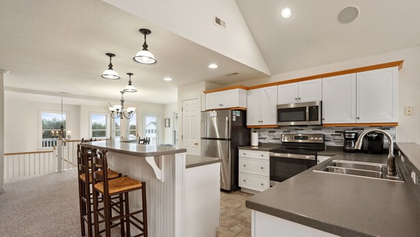 A modern kitchen with white cabinetry, stainless steel appliances, and a central island with bar stools. - Peace of Paradise: Private Pool, Hot Tub and Great Currituck Club amenities! (Corolla)