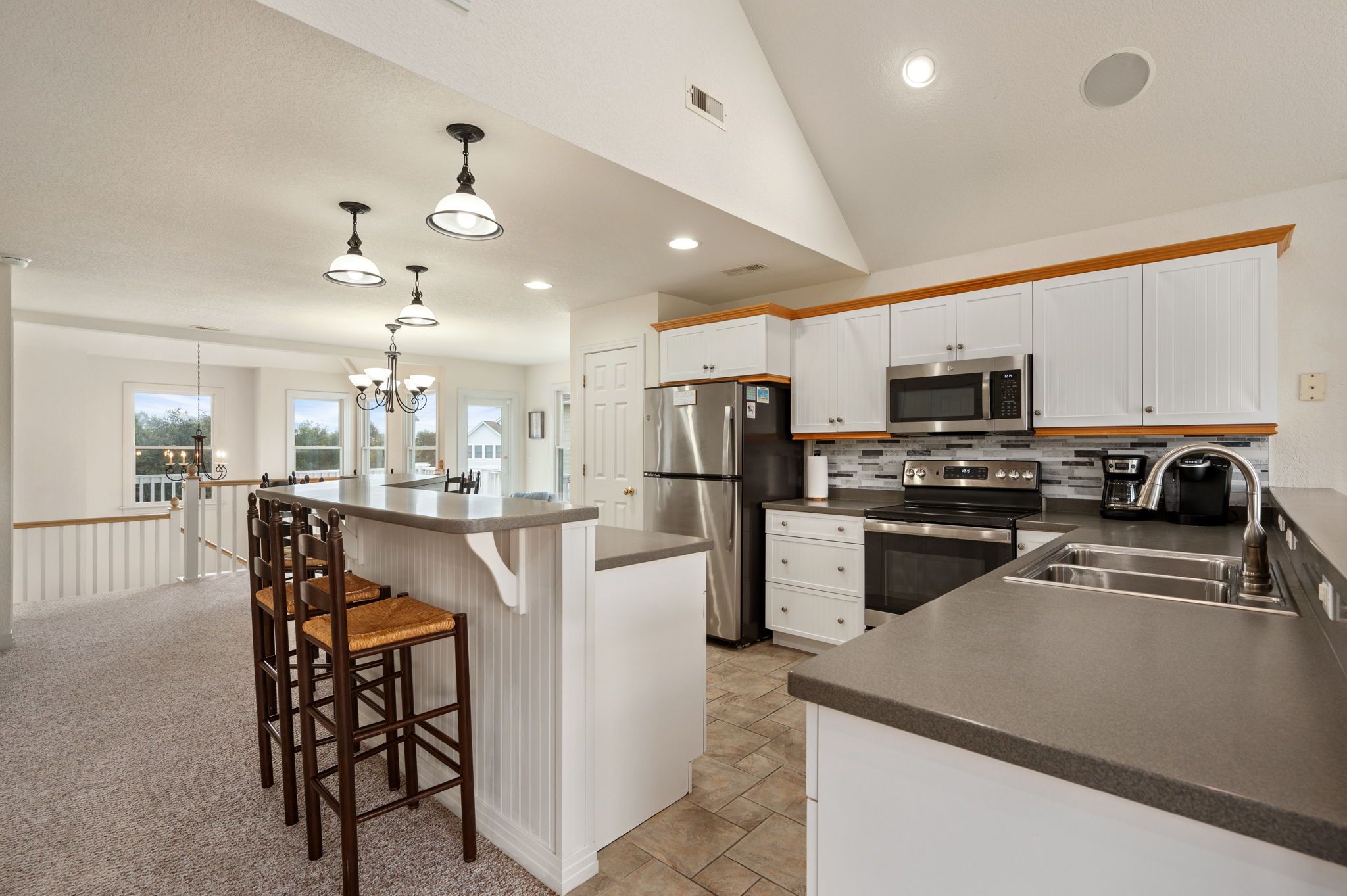 A modern kitchen with white cabinetry, stainless steel appliances, and a central island with bar stools.