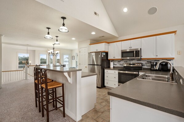 A modern kitchen with white cabinetry, stainless steel appliances, and a central island with bar stools.