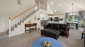 A spacious living area with a staircase, a black leather sofa, a dining table with chairs, and a kitchen in the background. - Peace of Paradise: Private Pool, Hot Tub and Great Currituck Club amenities! (Corolla)