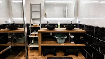 Ein modernes Badezimmer mit drei schwarzen Waschbecken, Holzregalen und einer Duschkabine aus Glas.