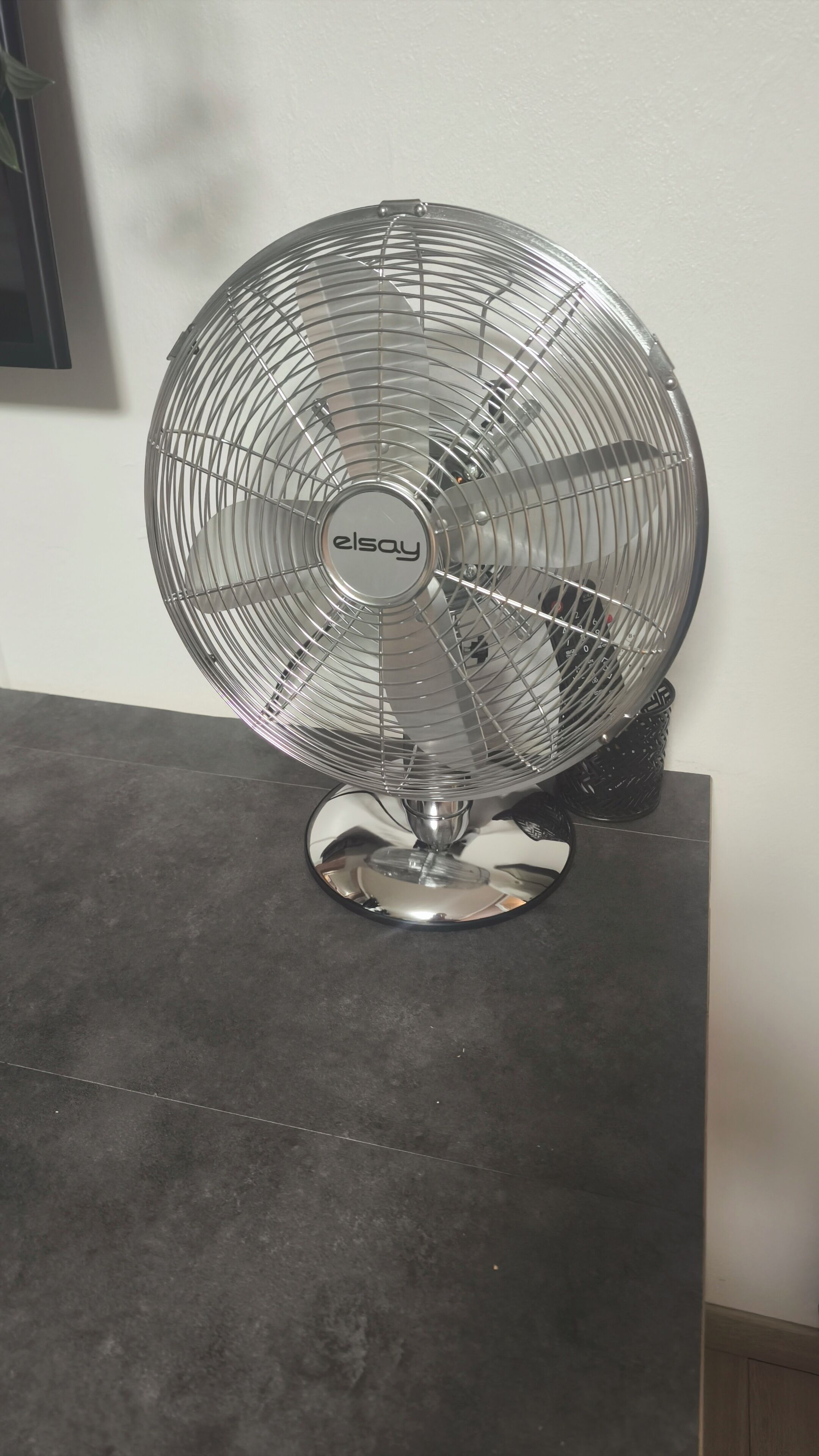 A standing fan with a metallic base on a dark surface.