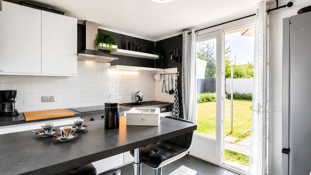 A modern kitchen with a central island, black and white cabinetry, and a view to the outdoors.