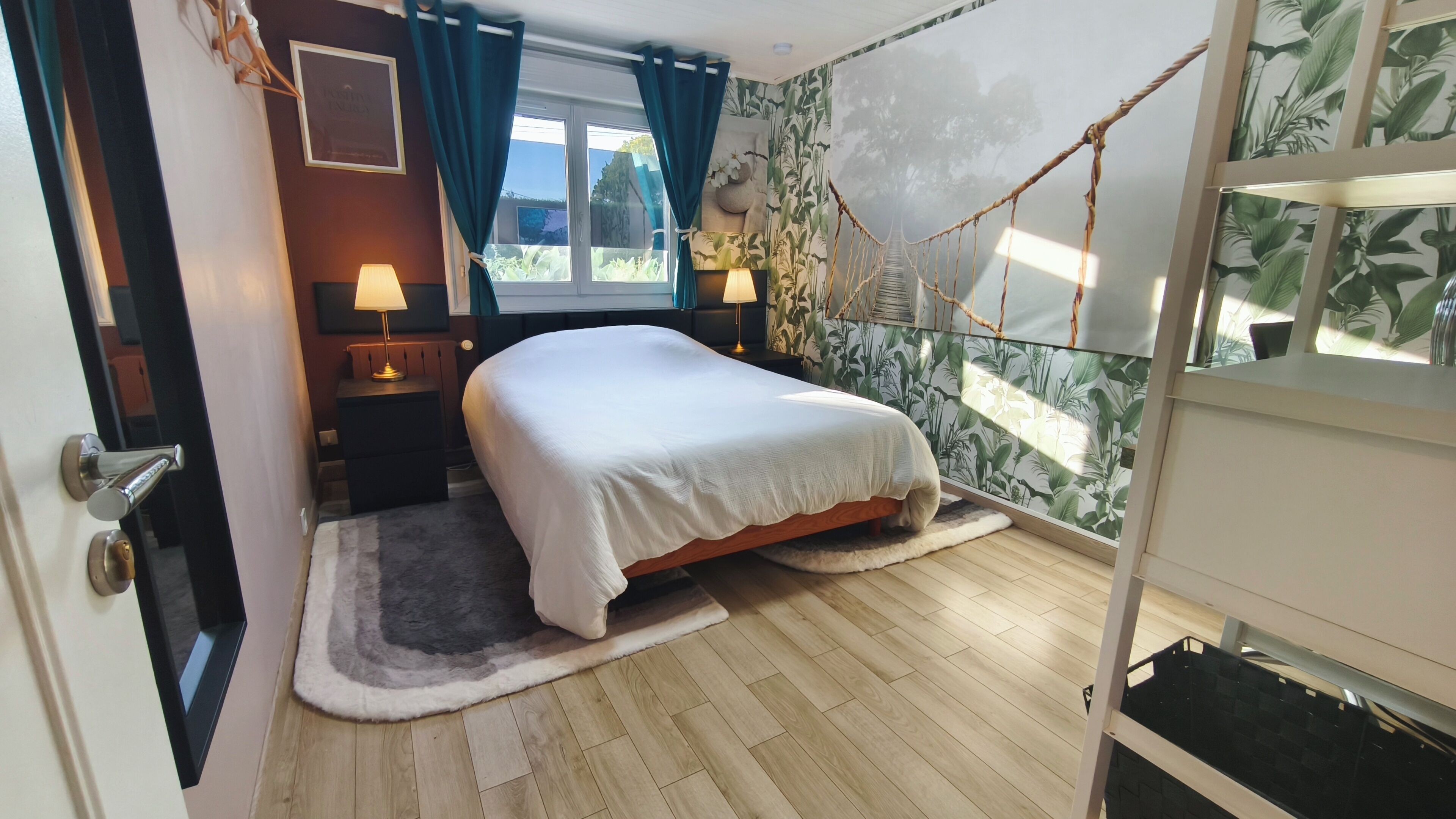 A bedroom with a bed, a nightstand, a lamp, a window with curtains, a view of greenery outside, and a rope swing.
