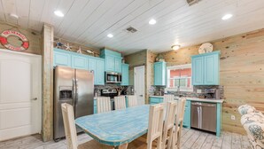 Una cocina con gabinetes color turquesa, un refrigerador de acero inoxidable y una mesa de comedor de madera con sillas.
