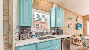 Cocina con armarios turquesa, lavavajillas de acero inoxidable y salpicadero de azulejos.