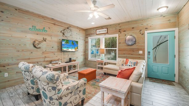Una habitación acogedora con paredes de madera, ventilador de techo, televisor, sofá, mesa de centro y una puerta.