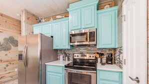Una cocina con gabinetes color turquesa, electrodomésticos de acero inoxidable y un salpicadero de azulejos.