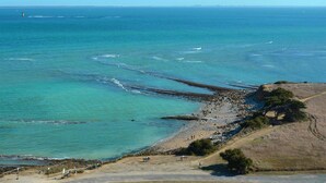 Un paisaje costero con playa, costa rocosa y un faro a lo lejos.