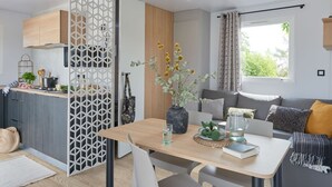 Una cocina moderna con encimera de madera, zona de comedor con mesa y sillas, y sala de estar con sofá y cojines.