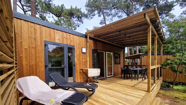 Una terraza de madera con dos sillones, una mesa y un área de estar cubierta.