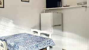 A room with a table covered in a patterned tablecloth, a white chair, a white cabinet, a television on a shelf, and framed pictures on the wall. - RM10 - Senigallia, two-room apartment facing the sea (Senigallia)
