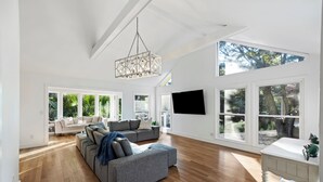 A spacious living room with a large gray sectional sofa, wooden flooring, and a modern chandelier. - Great FAMILY home in Wild Dunes, Pond View, Modern, Minutes to Beach, Rent the Golf Cart! (Isle Of Palms)