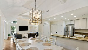 A modern kitchen with white cabinetry, a central island, and a dining area with a large table and chairs. - Great FAMILY home in Wild Dunes, Pond View, Modern, Minutes to Beach, Rent the Golf Cart! (Isle Of Palms)