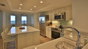 A modern kitchen with white cabinetry, stainless steel appliances, and a large island with seating. - Peaceful Paradise by the Sea | Inlet #1103 (New Smyrna Beach)