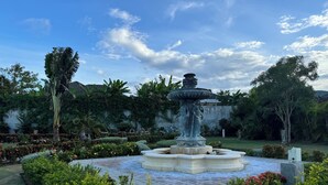 Un giardino con una fontana al centro, circondato da siepi curate e piante fiorite.