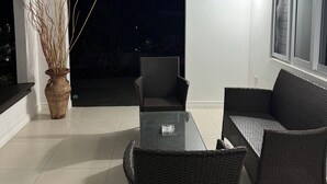 Un'area salotto all'aperto riparata, con mobili in rattan, una pianta in vaso e una ventola a soffitto.