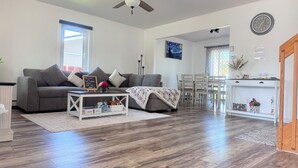 Un salon moderne avec un canapé gris, une table basse et un coin repas comprenant une table et des chaises blanches.
