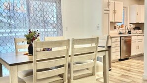 Un coin repas avec des chaises et une table en bois, une cuisine avec des meubles blancs et un plancher en bois.