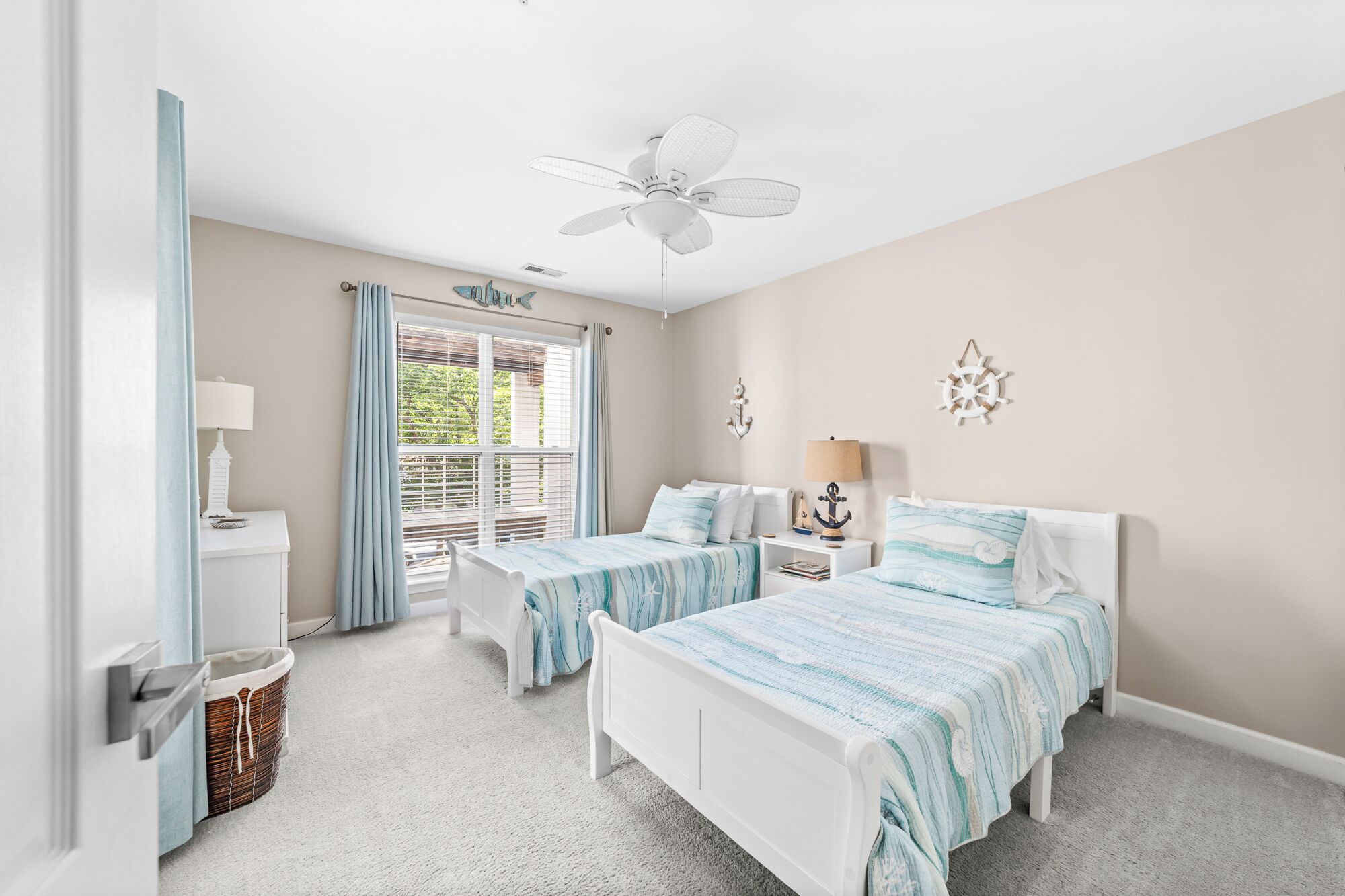 A bedroom with two beds, a ceiling fan, a window with blinds, and nautical-themed decor.