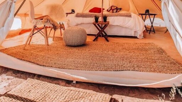 A spacious tent with a bed, pillows, a chair, and a small table. - Yellowstone Glamping (Island Park)