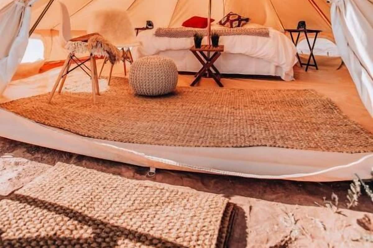 Ein geräumiges Zelt mit einem Bett, Kissen, einem Sessel und einem kleinen Tisch.