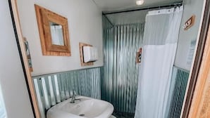 A compact bathroom with a sink, toilet, and shower curtain. - Yellowstone Glamping (Island Park)