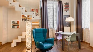 Une pièce moderne avec un fauteuil turquoise, une table à manger, une lampe, un escalier et des œuvres d’art murales.