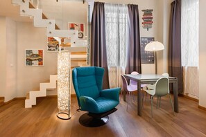 Una habitación moderna con una silla verde azulada, una mesa de comedor, una lámpara, una escalera y decoración en la pared.