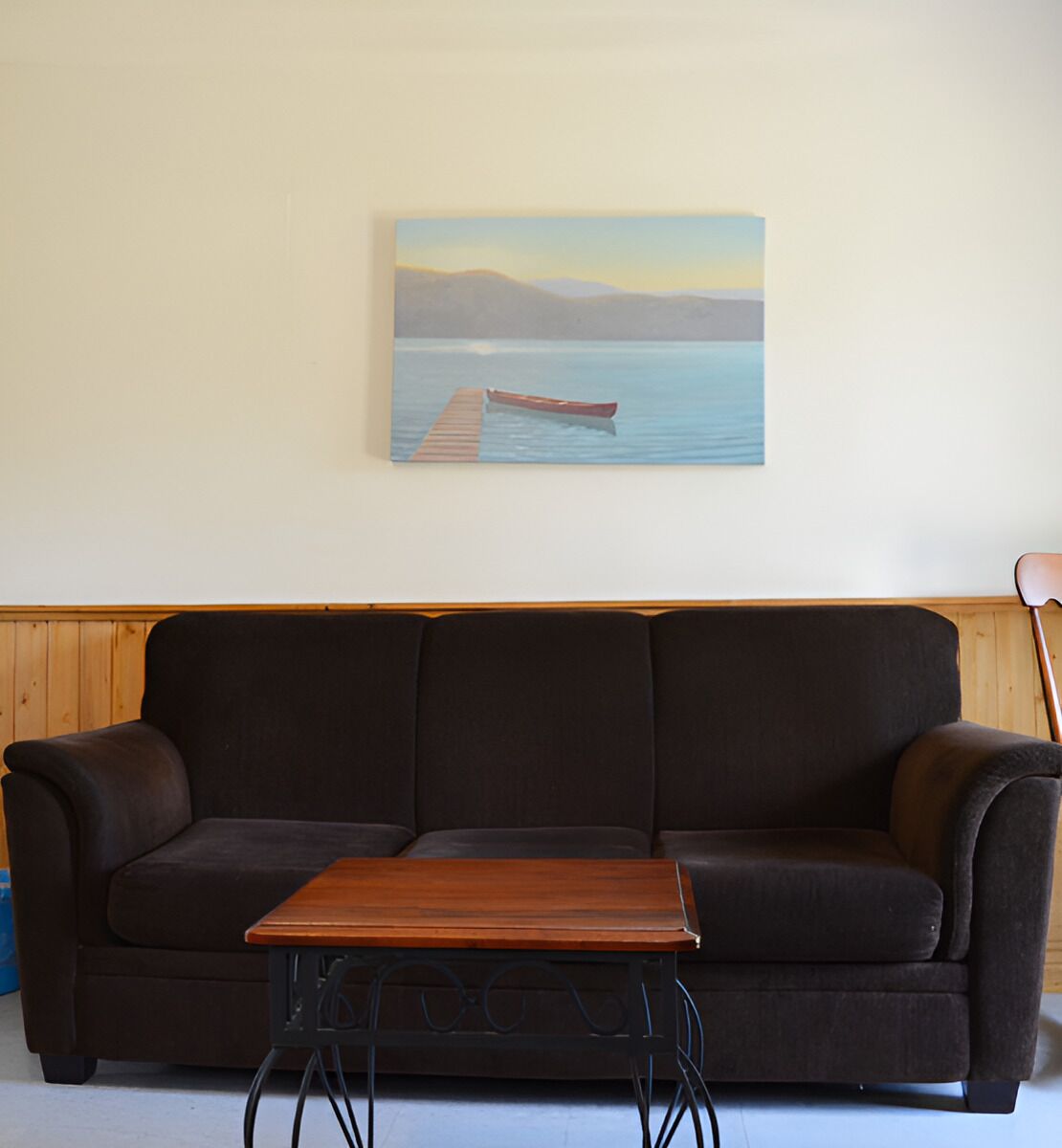 A dark brown sofa with a wooden coffee table in front, a wooden wall paneling, and a painting of a boat on a dock.