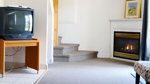 Un salon avec un téléviseur posé sur un meuble en bois, une cheminée et un escalier menant à une autre pièce.