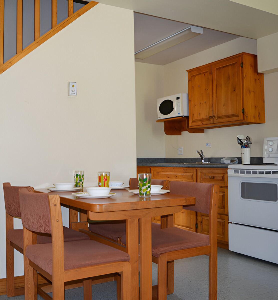 A dining area with wooden chairs and a table set for four, a microwave, and a stove in the kitchen area.